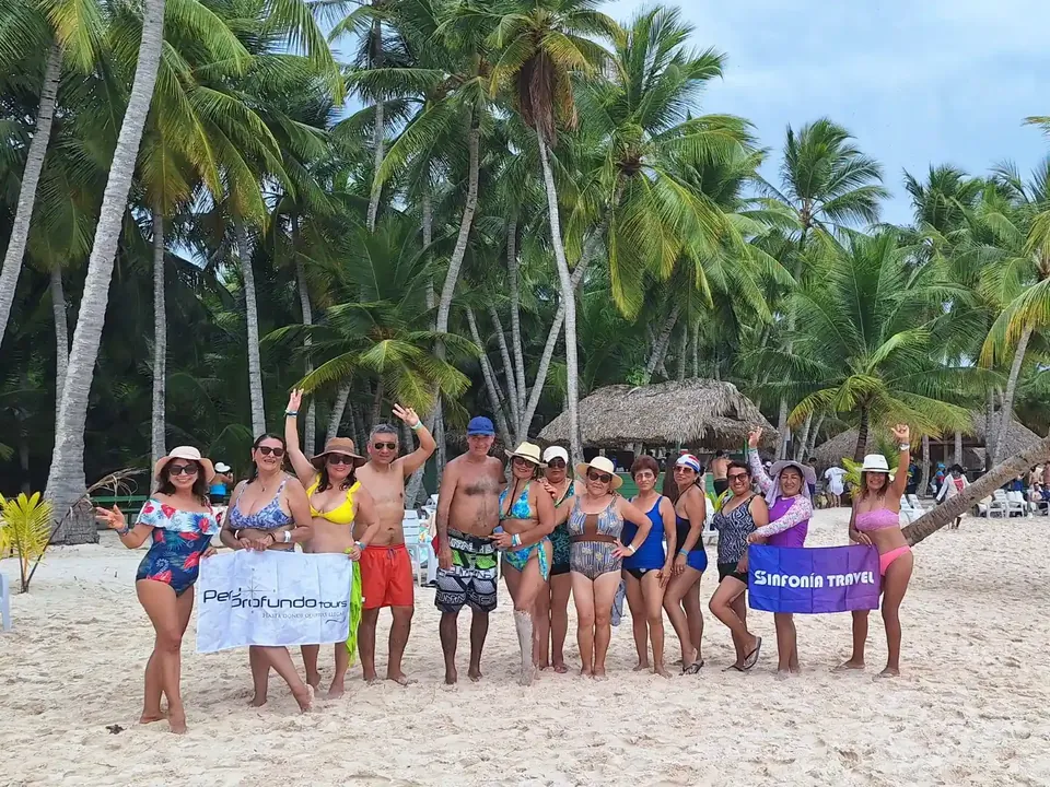 Grupo de viajeros de Sinfonía Travel en la playa sosteniendo una banderola